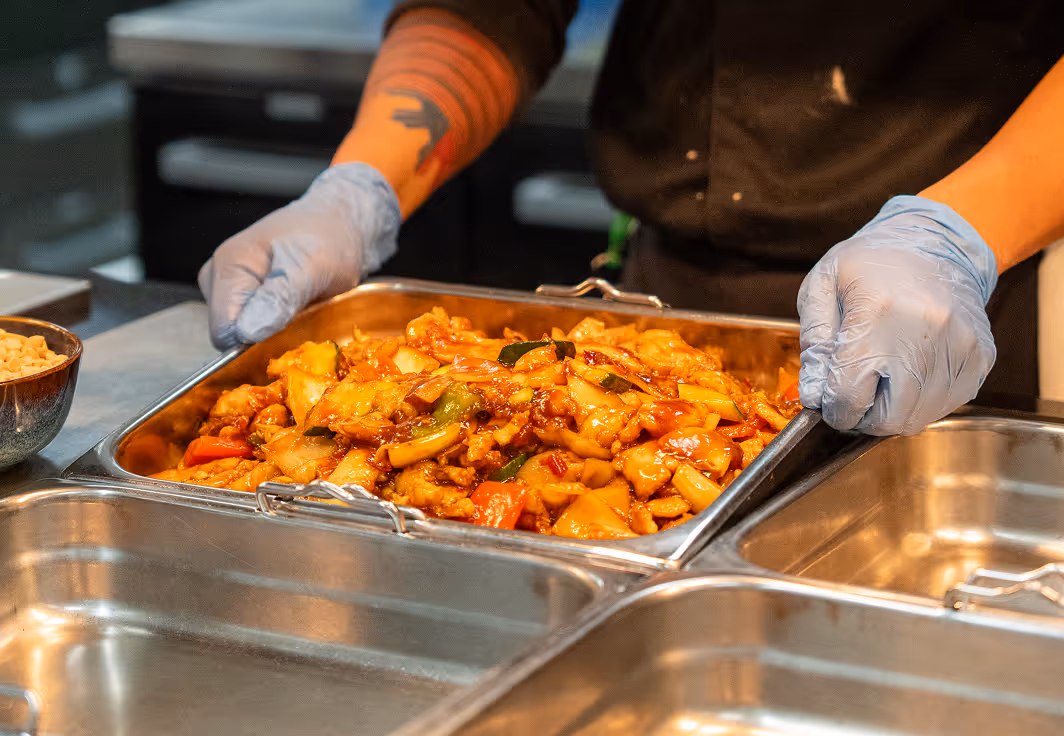 Gloved hands holding a tray of stir-fried food.