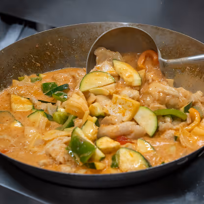 Spoon stirring a curry with vegetables in a pan.
