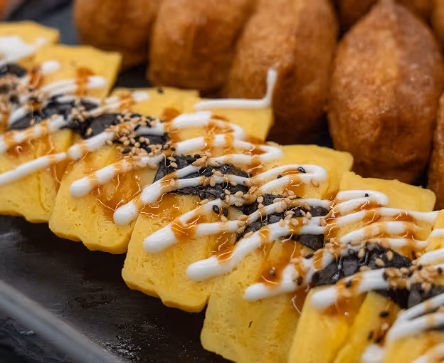 Tamago sushi with sauce and sesame, next to inari sushi.