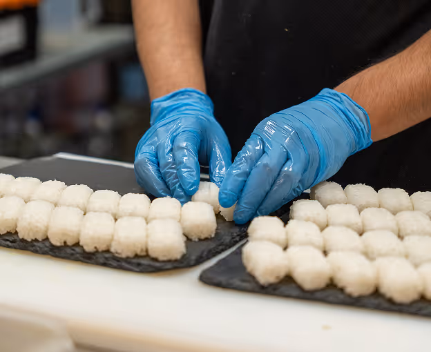 Person shaping sushi rice portions with gloved hands.